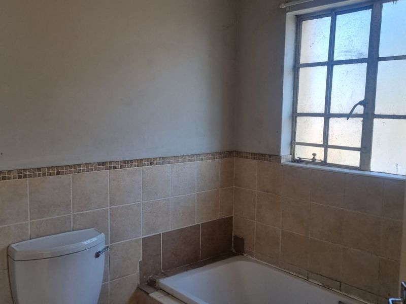A dated bathroom featuring a bathtub, toilet, and partial wall tiling, currently in need of renovation and cosmetic repairs.