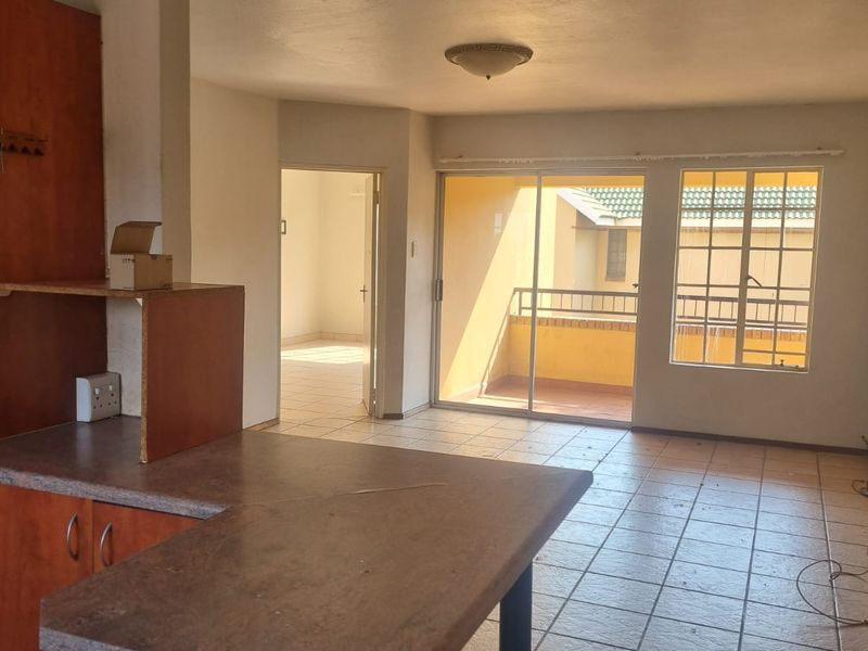 Open-plan living area featuring tiled floors, built-in kitchen cabinetry, and a sliding door leading to a balcony, offering a blank canvas for renovation.