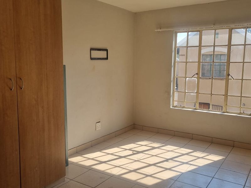 A vacant bedroom featuring tiled flooring, a built-in wardrobe, and a window with security bars, offering a blank canvas for personalization.