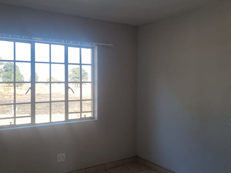 A vacant bedroom featuring tiled flooring, a built-in cupboard, and a grid-pattern window with natural light.