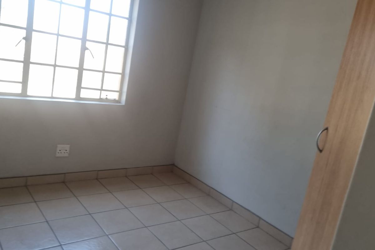 A simple, empty bedroom featuring tiled flooring, a built-in wardrobe, and a window with security bars.