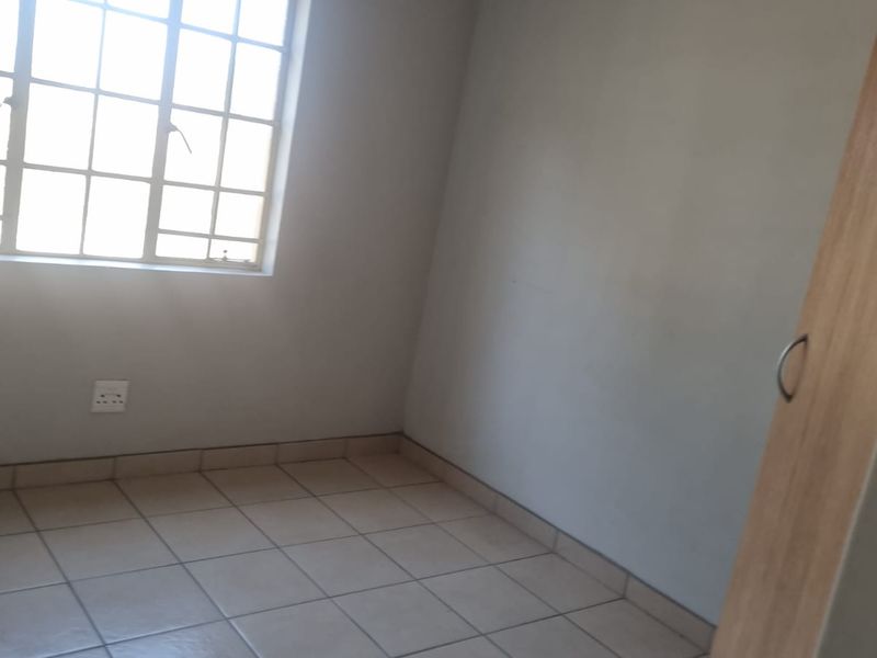 A simple, empty bedroom featuring tiled flooring, a built-in wardrobe, and a window with security bars.
