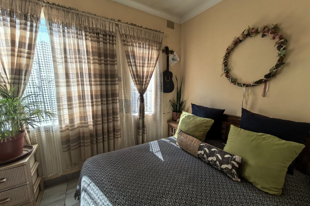 A bedroom featuring natural light through large windows, with visible wear on wall finishes and paintwork requiring maintenance.