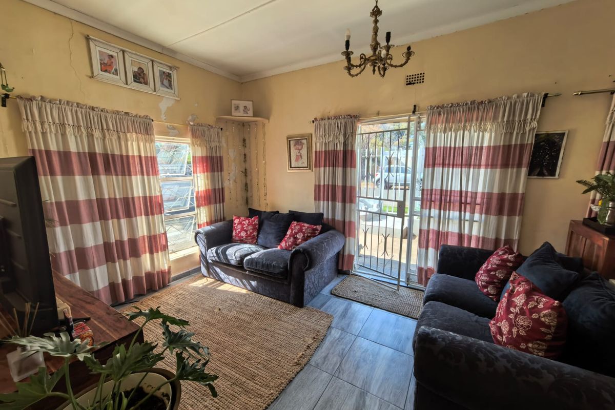 A living room featuring tiled flooring, a security gate, and a ceiling light fixture, showing signs of wear including cracked plaster and peeling paint.