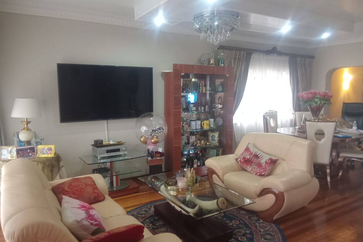 A comfortable living room featuring polished hardwood flooring, decorative ceiling cornices, and a central crystal chandelier, creating a warm and inviting atmosphere.