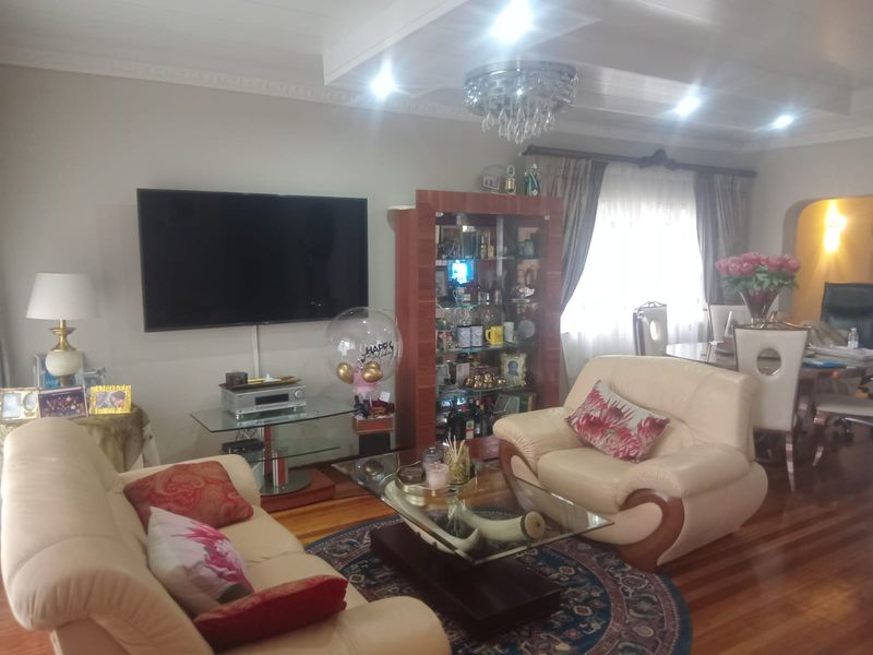 A comfortable living room featuring polished hardwood flooring, decorative ceiling cornices, and a central crystal chandelier, creating a warm and inviting atmosphere.