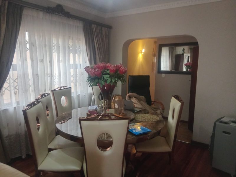 A dining room featuring hardwood flooring, decorative ceiling cornicing, and a classic archway leading to an adjacent space.