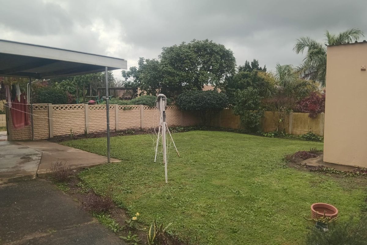 A rear garden area featuring a lawn, concrete boundary walls, and a covered patio space.