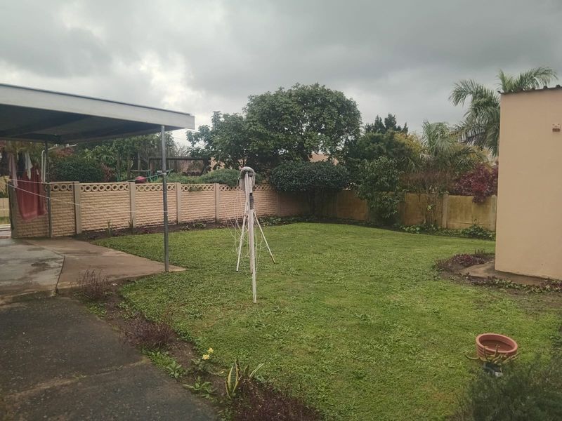 A rear garden area featuring a lawn, concrete boundary walls, and a covered patio space.