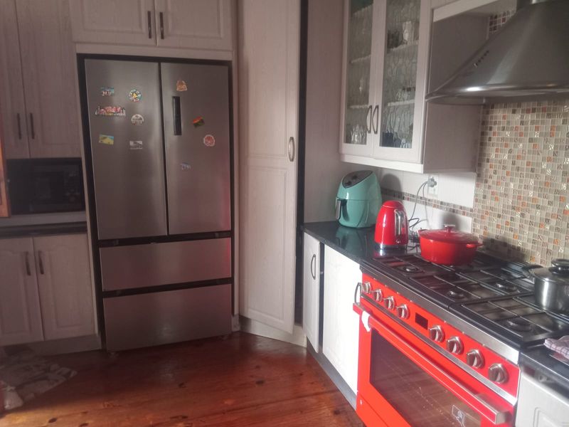 A functional kitchen featuring white cabinetry, a mosaic tile backsplash, hardwood flooring, and a prominent red gas stove with an overhead extractor fan.