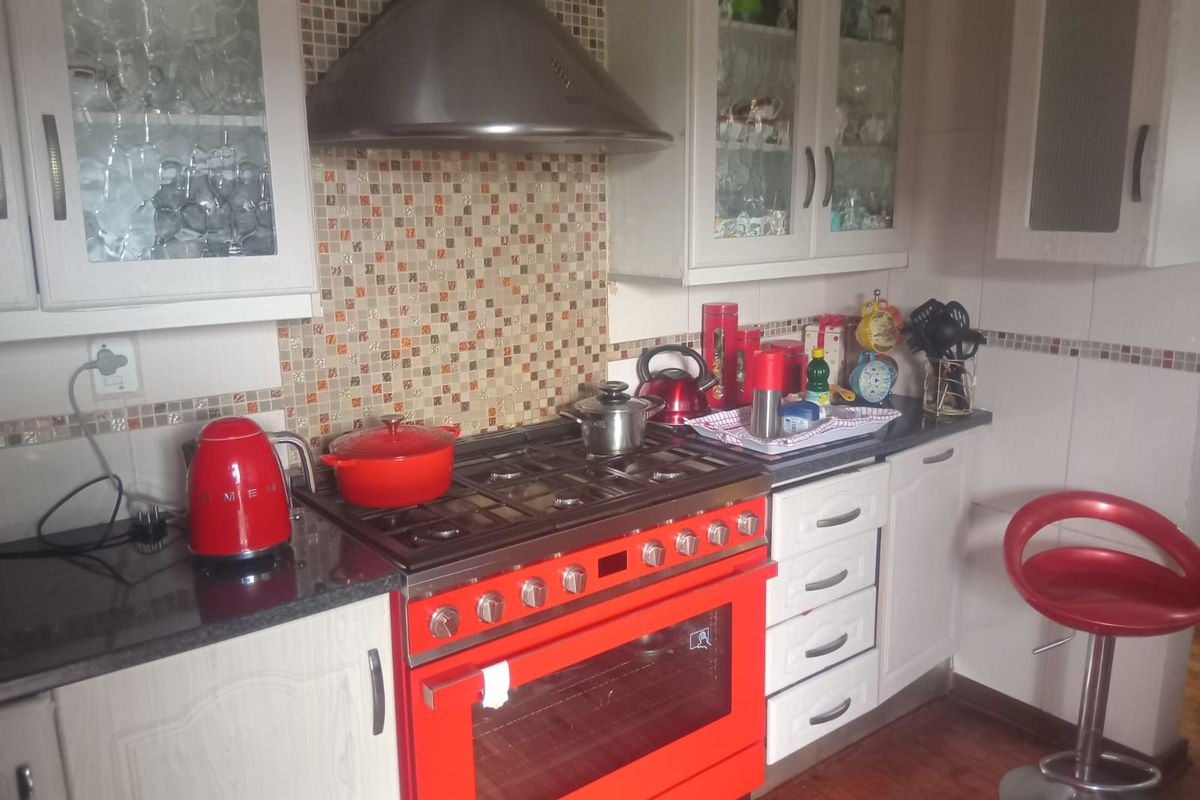 A functional kitchen featuring a prominent red gas stove, extractor fan, mosaic tile backsplash, and ample cabinetry with glass-fronted upper units.