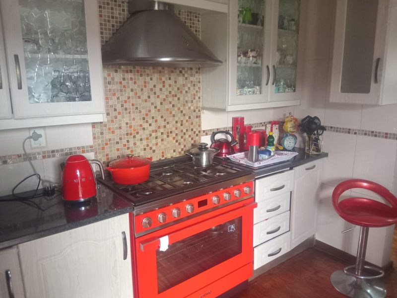 A functional kitchen featuring a prominent red gas stove, extractor fan, mosaic tile backsplash, and ample cabinetry with glass-fronted upper units.