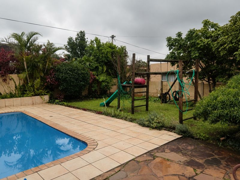 Outdoor pool area featuring a tiled pool surround, stone patio, and a landscaped garden with established trees and boundary walling.