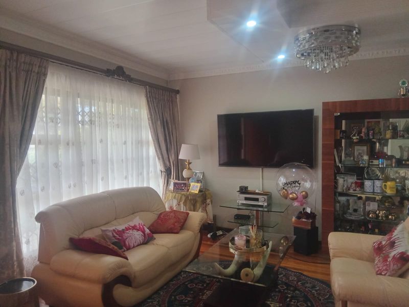 A comfortable living room featuring timber flooring, decorative ceiling cornices, recessed lighting, a crystal chandelier, and a built-in display cabinet.