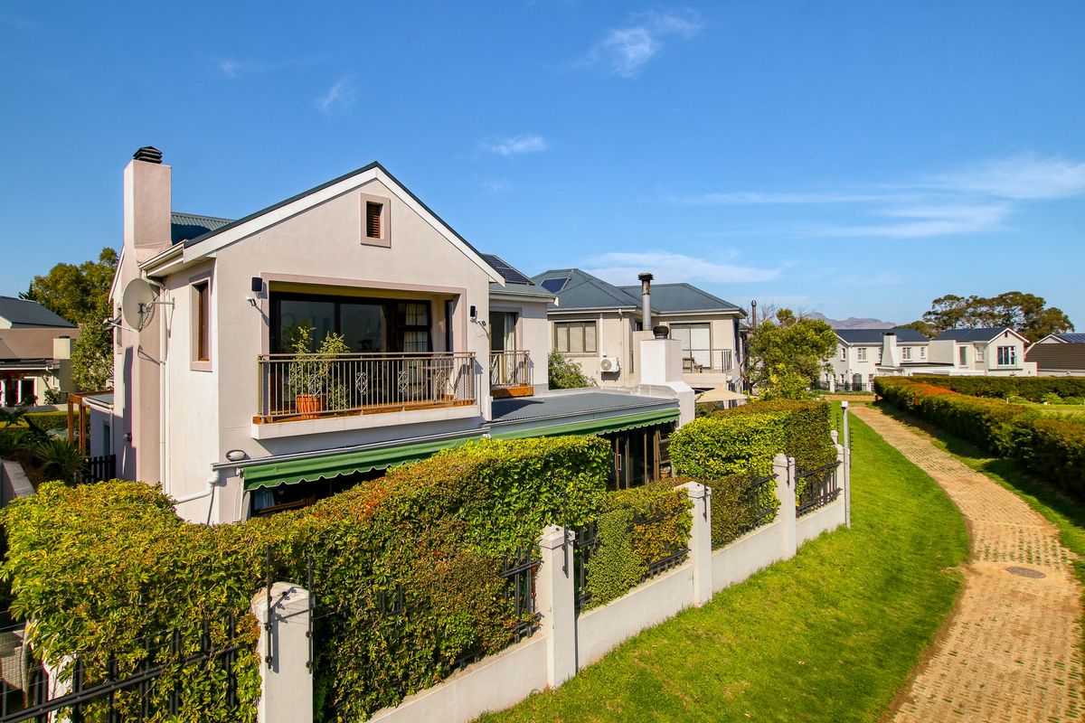 Rear view of a townhouse featuring a balcony, retractable awning, and well-maintained garden with a paved walkway in a residential estate setting.