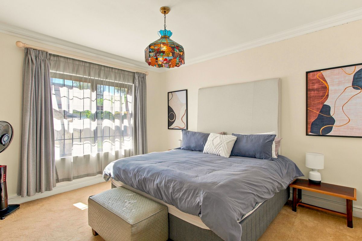 A well-maintained bedroom featuring neutral wall tones, carpeted flooring, crown molding, and a window fitted with security bars.