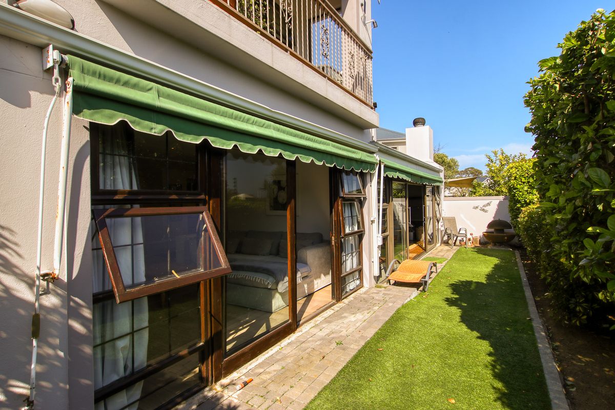 Rear exterior view of the townhouse featuring a paved walkway, artificial lawn, and retractable awnings over the sliding glass doors.