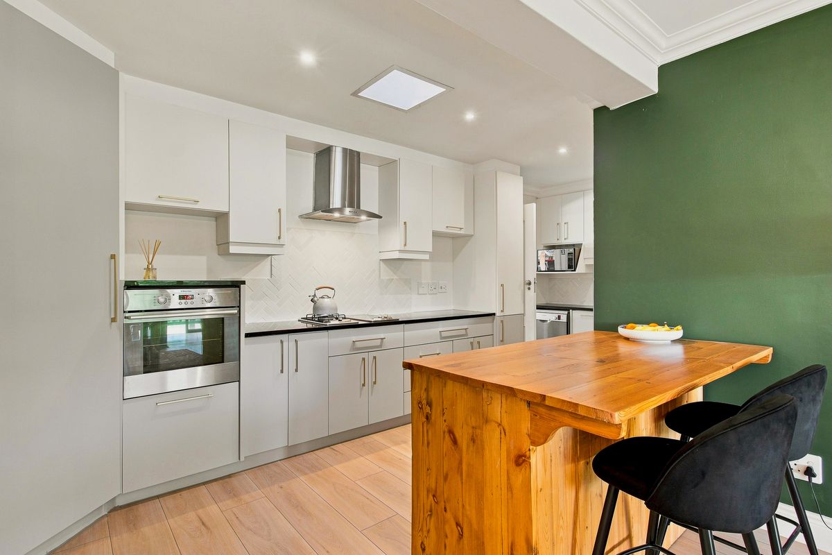 Modern kitchen featuring white cabinetry, a tiled backsplash, built-in oven, extractor fan, and a wooden breakfast bar island.