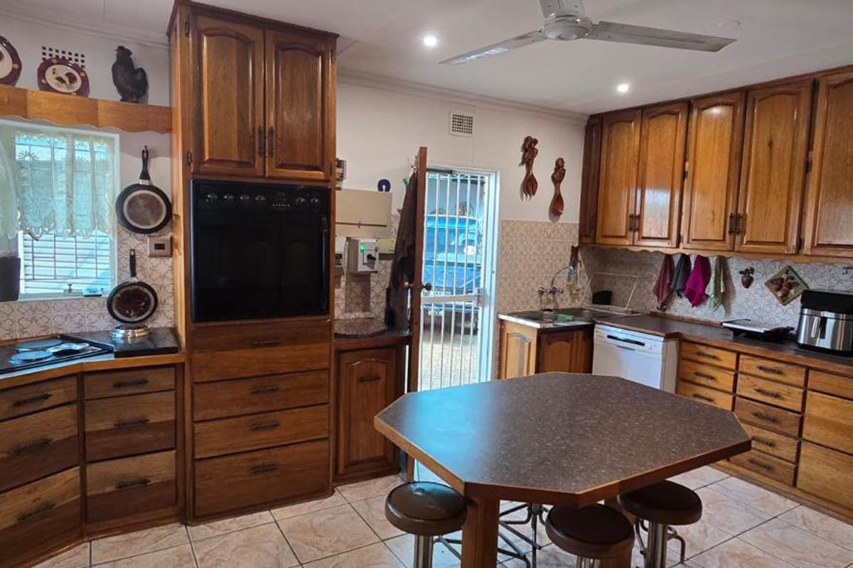 A traditional kitchen featuring extensive wooden cabinetry, built-in oven, cooktop, tiled backsplash, and a central island with seating.