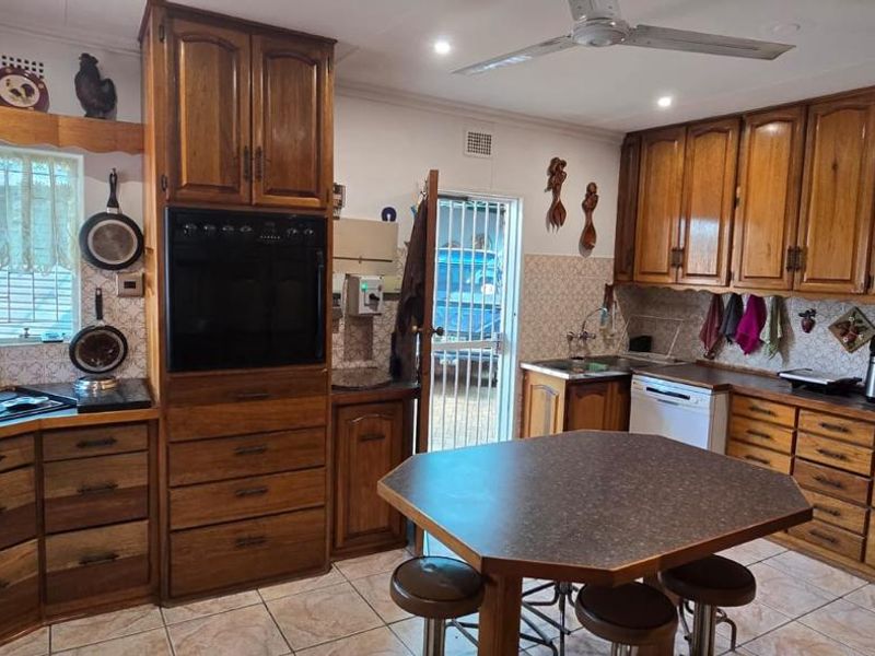 A traditional kitchen featuring extensive wooden cabinetry, built-in oven, cooktop, tiled backsplash, and a central island with seating.