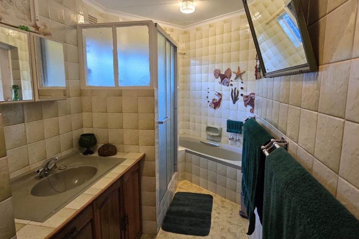 A dated bathroom featuring a vanity cabinet, integrated sink, shower enclosure, and bathtub with full-height wall tiling.