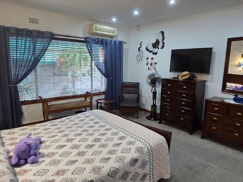 A spacious bedroom featuring carpeted flooring, recessed downlighting, and a wall-mounted air conditioning unit for climate control.