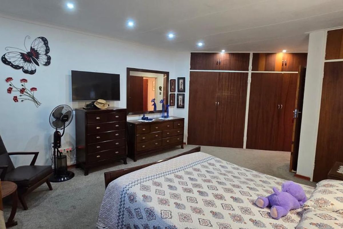 Spacious bedroom featuring extensive built-in wooden cupboards, recessed downlighting, and neutral carpeting, offering a functional and well-maintained living space.