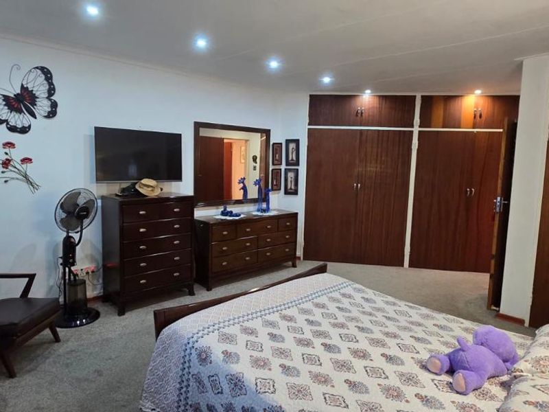 Spacious bedroom featuring extensive built-in wooden cupboards, recessed downlighting, and neutral carpeting, offering a functional and well-maintained living space.