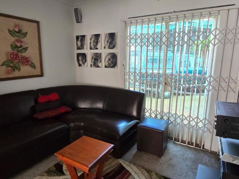 A living room featuring carpet flooring and a sliding glass door with a security gate providing access to the exterior.