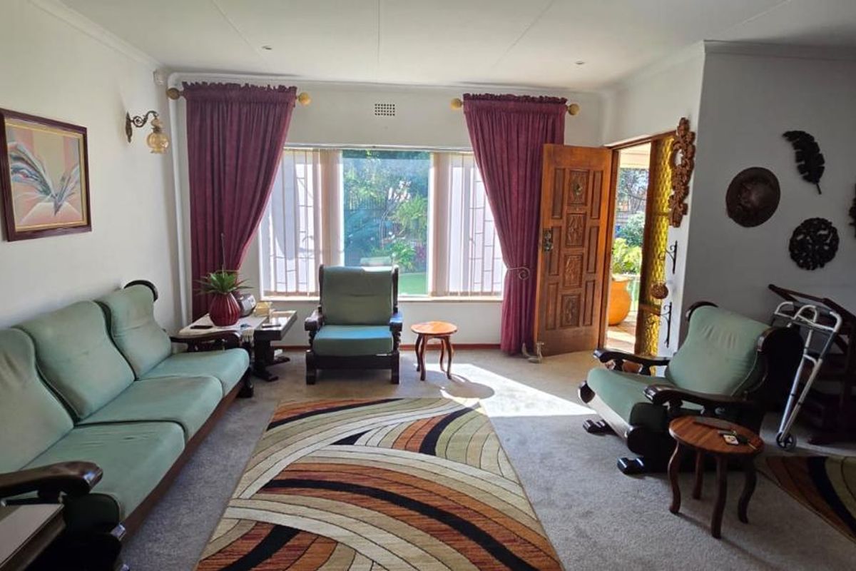 A spacious living room featuring coved ceilings, recessed lighting, and a large window with security bars, providing direct access to the outdoor area.