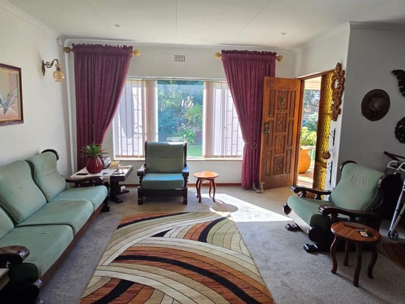 A spacious living room featuring coved ceilings, recessed lighting, and a large window with security bars, providing direct access to the outdoor area.