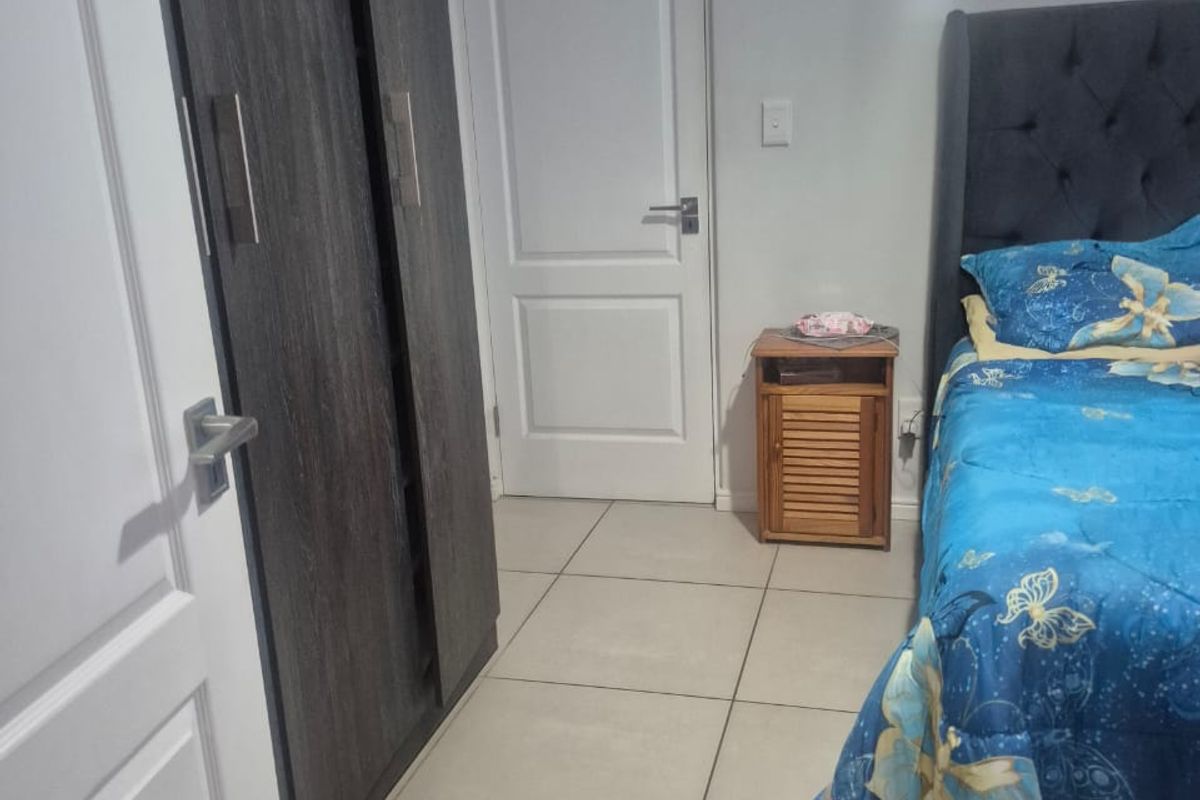 A bedroom featuring neutral tiled flooring and a dark wood-finish built-in wardrobe.