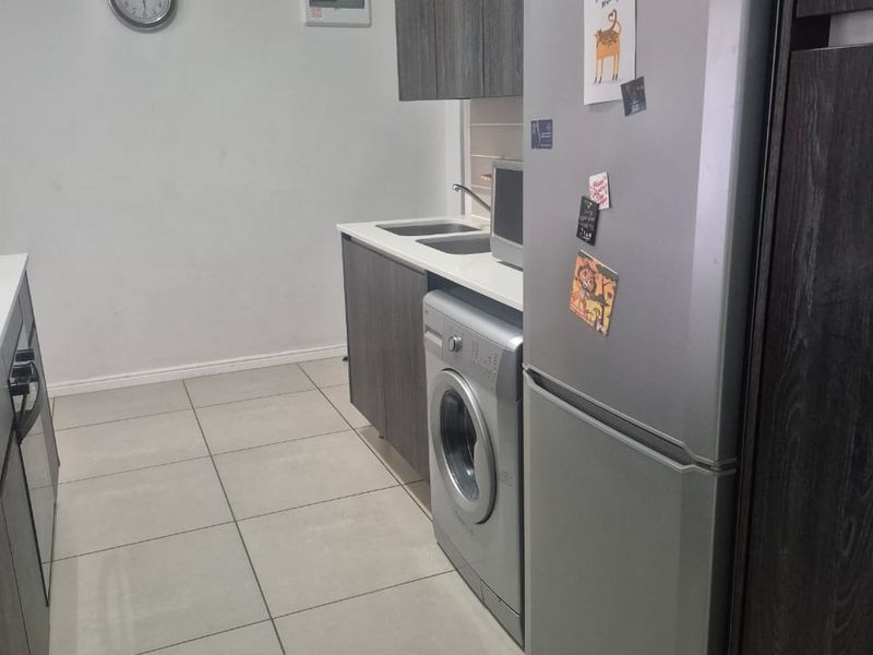 A functional kitchen featuring modern dark wood cabinetry, light countertops, tiled flooring, and integrated space for laundry appliances.