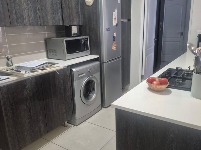 Modern kitchen featuring dark wood-grain cabinetry, stone countertops, a gas hob, and integrated space for laundry appliances.