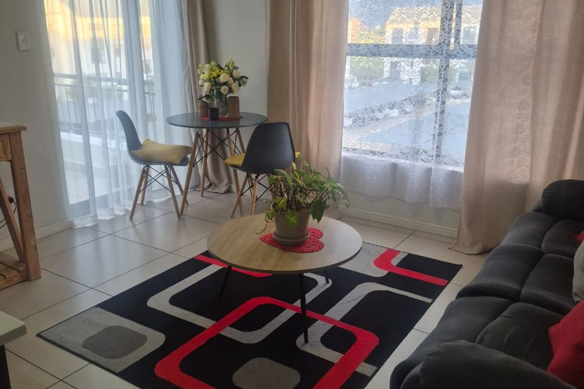 A bright living area featuring neutral tiled flooring, large windows, and a sliding glass door providing access to an outdoor space.