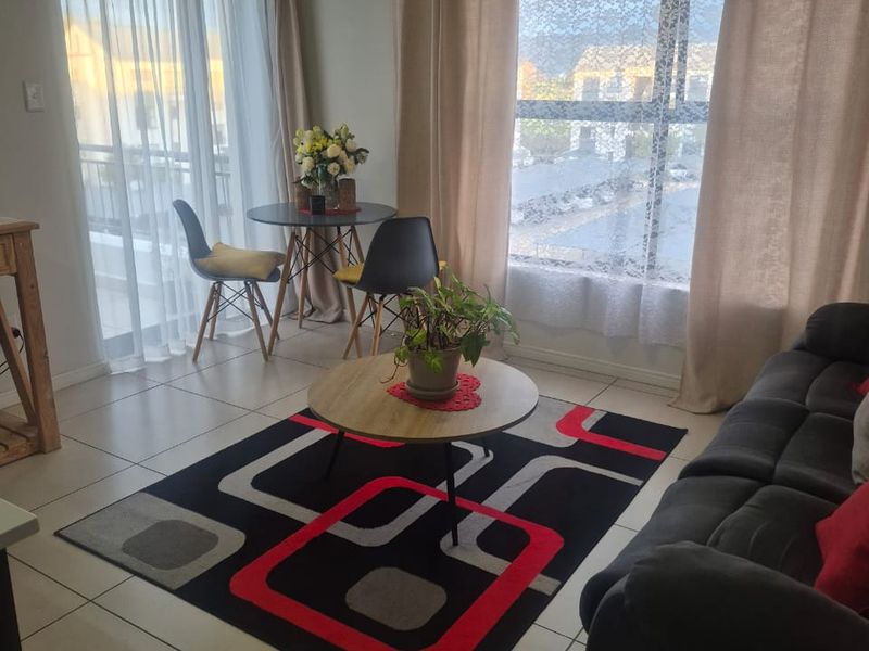 A bright living area featuring neutral tiled flooring, large windows, and a sliding glass door providing access to an outdoor space.