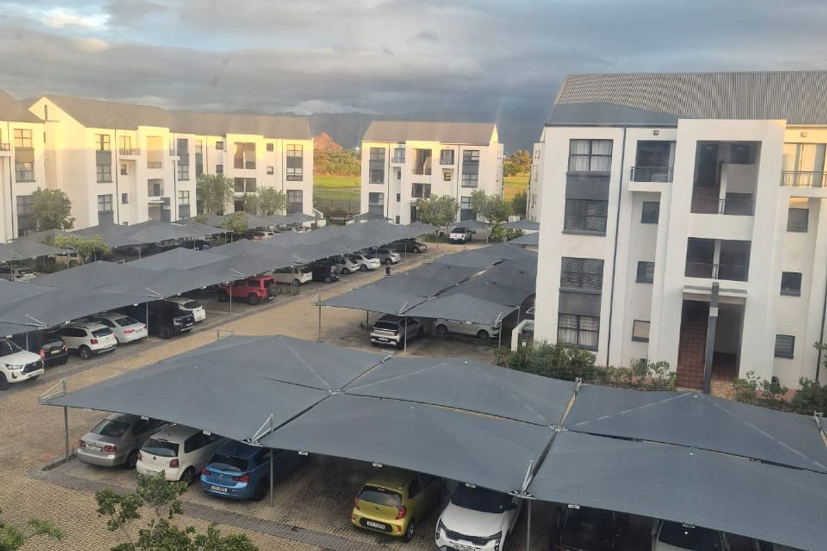 An elevated view of an apartment complex featuring paved parking areas with installed shade cloth carports and multi-story residential buildings.