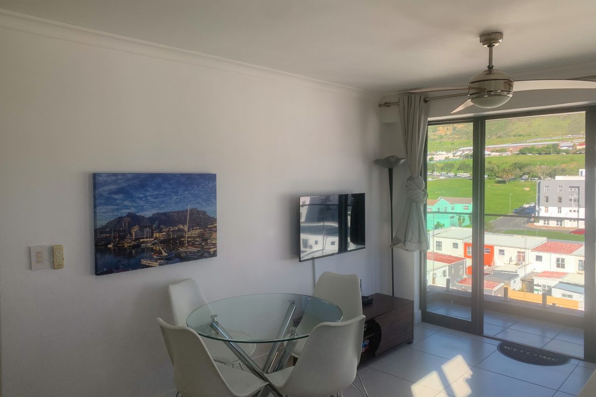 A bright living area featuring tiled flooring, a ceiling fan, and large sliding glass doors providing access to a balcony with scenic views.