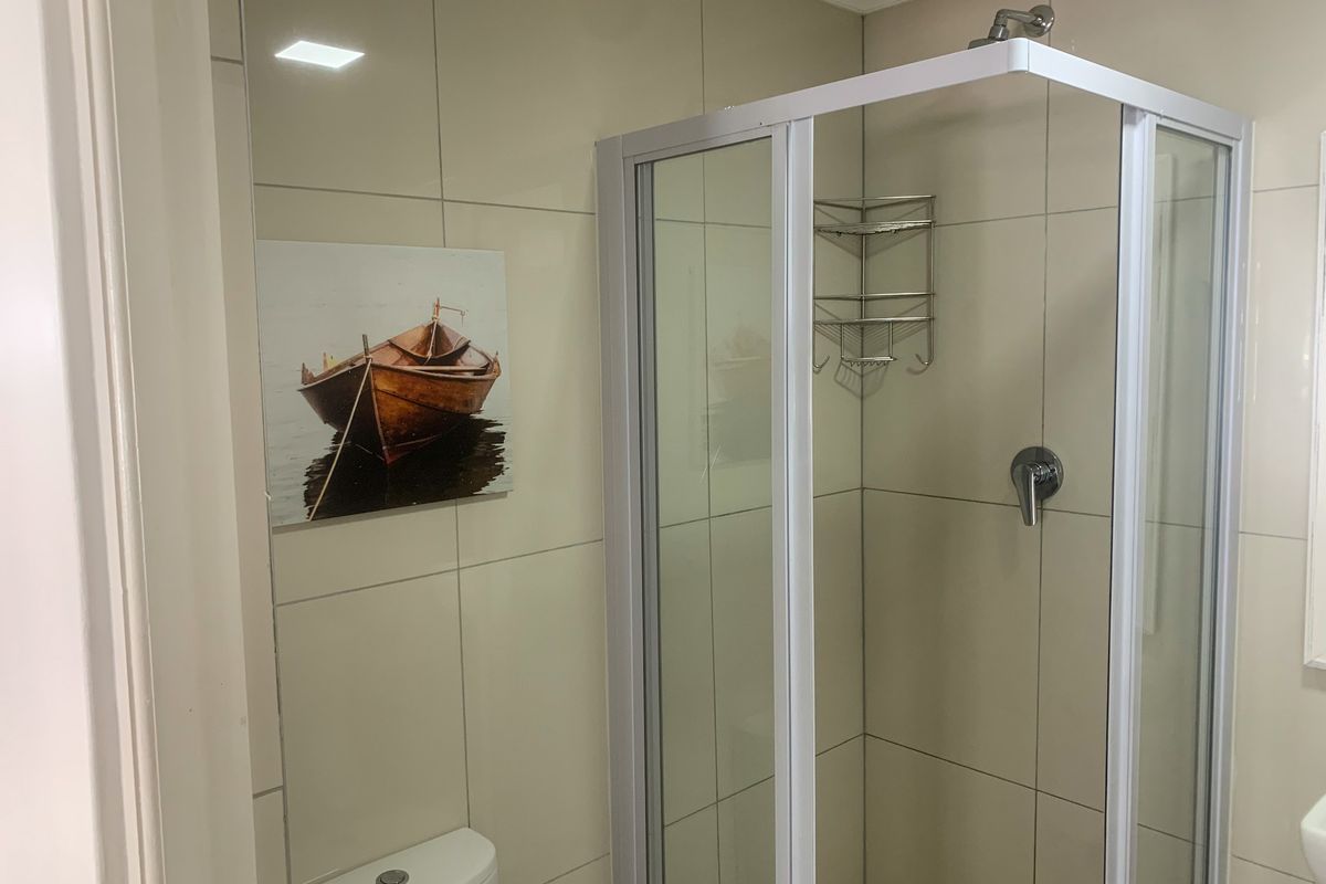 A clean, modern bathroom featuring a glass-enclosed shower, wall-mounted shower mixer, and a standard toilet with neutral ceramic wall tiling.