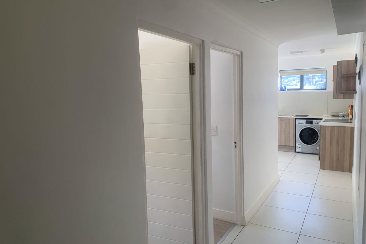 A bright hallway leading into an open-plan kitchen area featuring modern tiled flooring and neutral white walls.