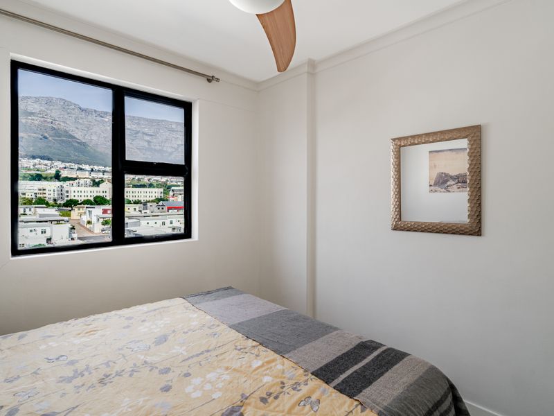 A bedroom featuring a ceiling fan and an aluminium window frame with a scenic mountain and city view.
