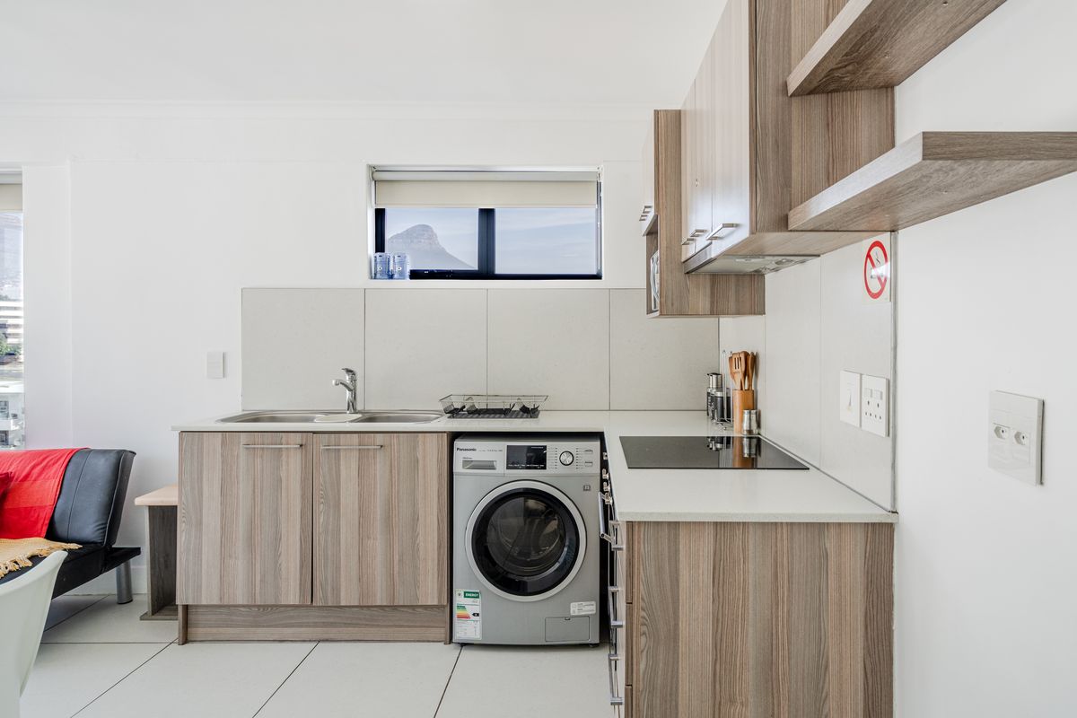 Modern compact kitchen featuring wood-grain cabinetry, integrated washing machine, electric cooktop, and sleek tiled backsplash with ample counter space.