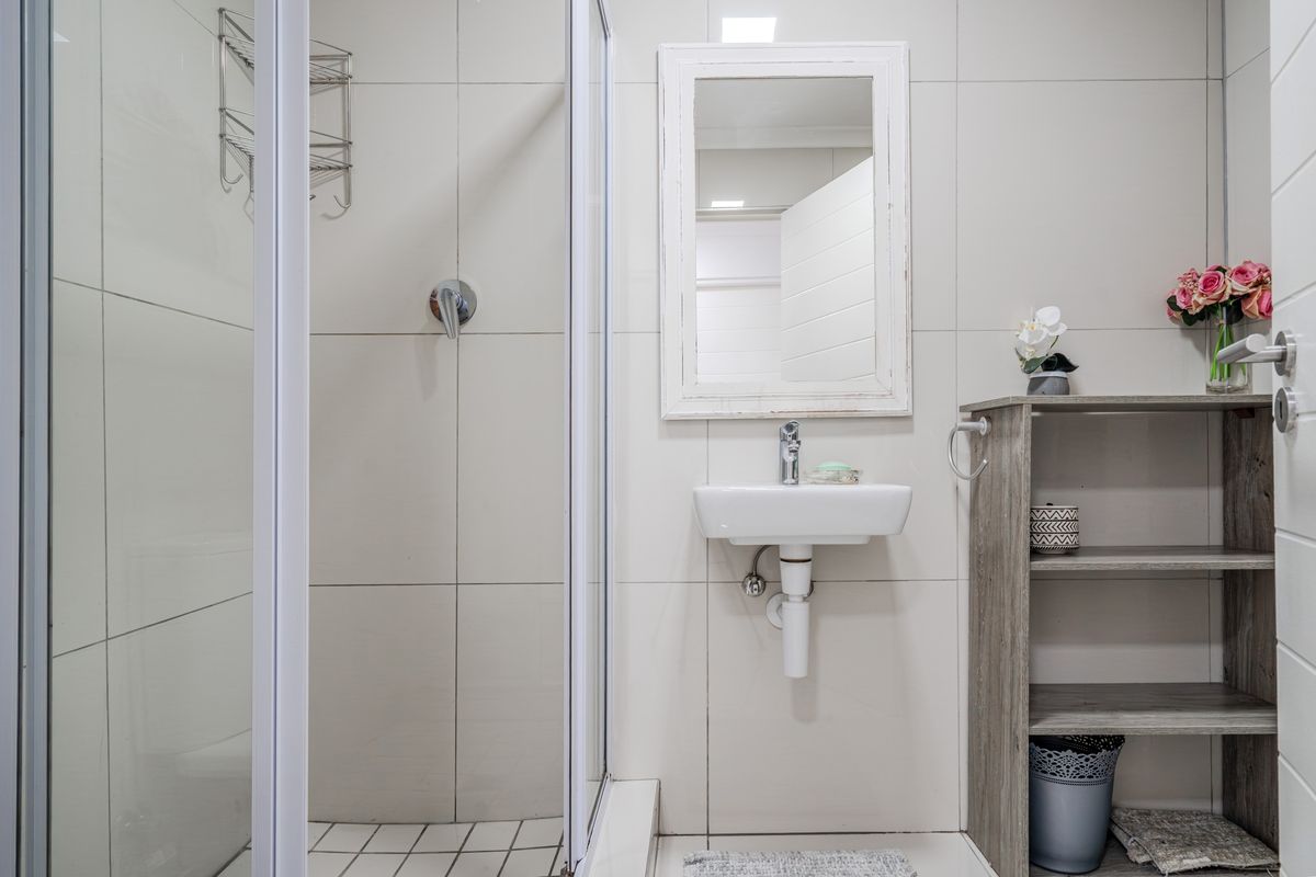 A compact, modern bathroom featuring a glass-enclosed shower, wall-mounted basin with chrome fixtures, and neutral wall tiling.
