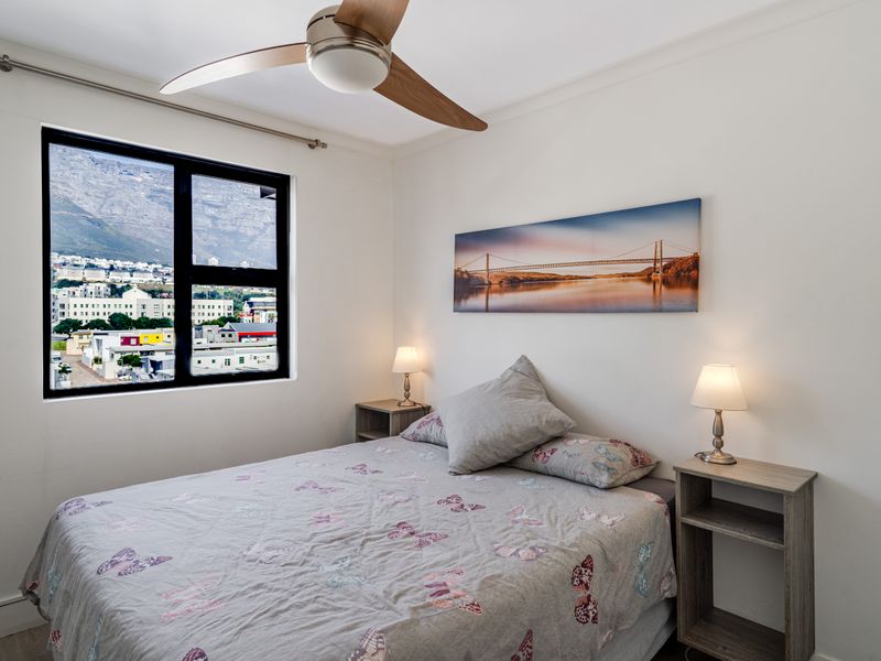 A well-maintained bedroom featuring a ceiling fan, neutral finishes, and a large window offering scenic mountain and urban views.