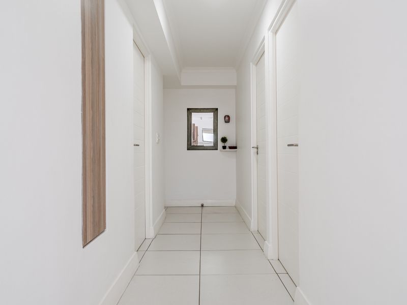 A clean, well-maintained hallway featuring neutral tiled flooring and multiple internal doors, providing access to various rooms within the apartment.