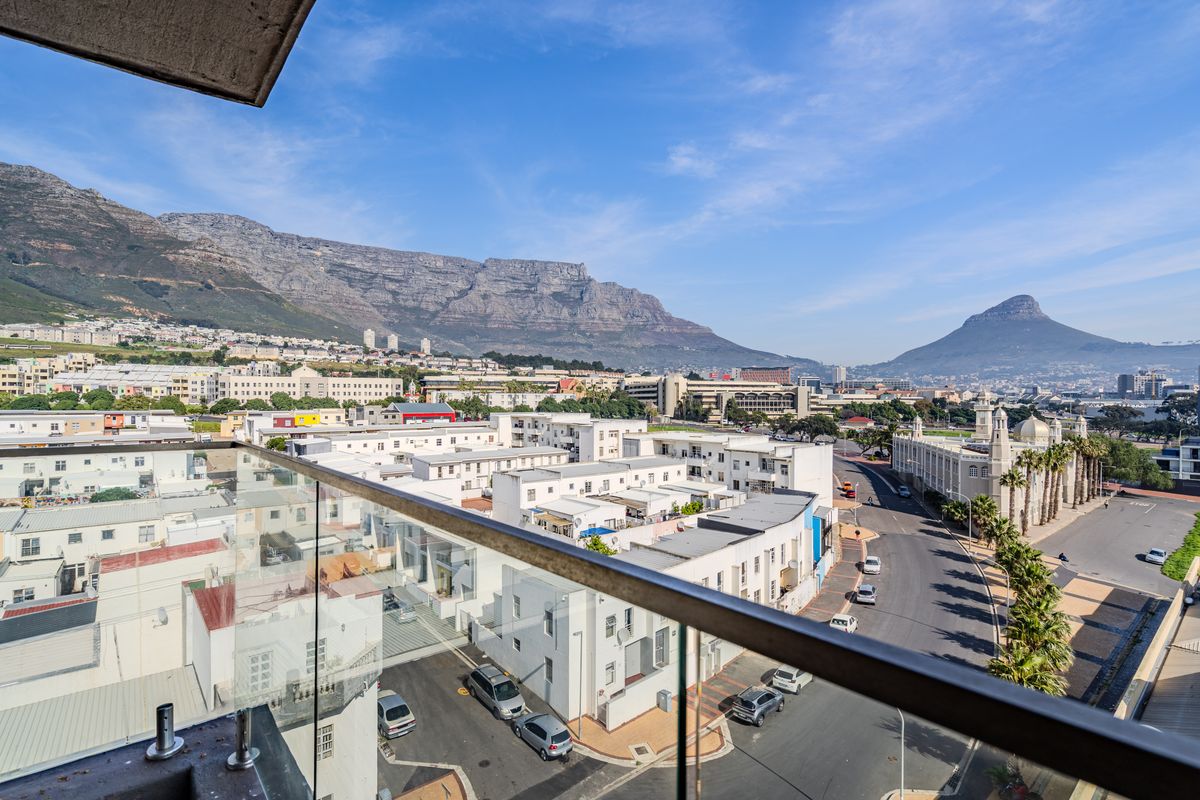 Elevated panoramic view overlooking the city, surrounding buildings, and iconic mountain ranges, captured from a modern apartment balcony with a glass balustrade.