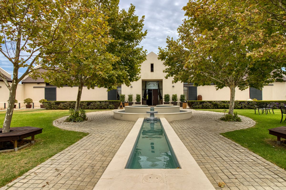A beautifully landscaped courtyard featuring a central water feature, paved pathways, and mature trees leading to the main building entrance.