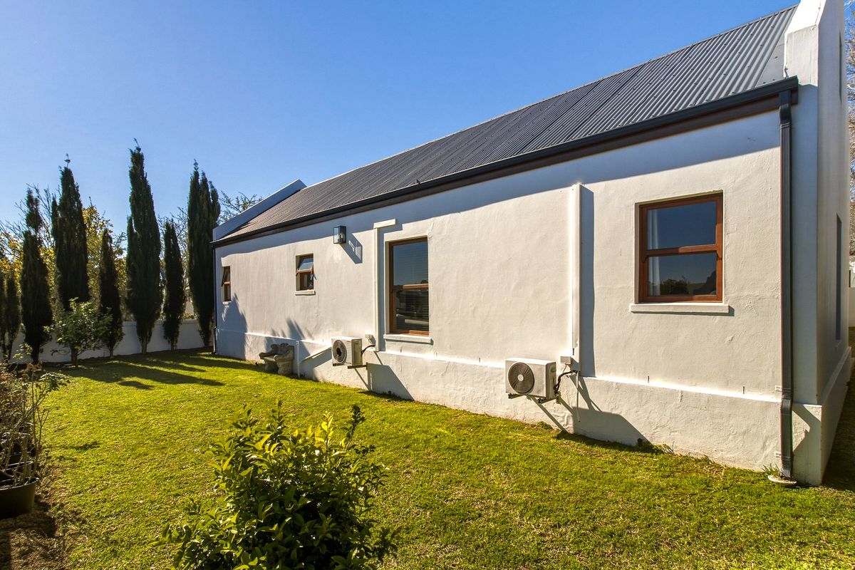 Rear view of the property featuring a well-maintained lawn, plastered exterior walls, corrugated metal roof, and mounted air conditioning units.