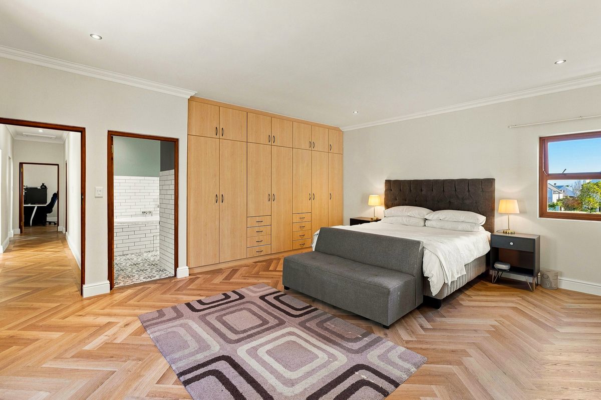 Spacious bedroom featuring high-quality herringbone timber flooring, extensive built-in cabinetry, and an en-suite bathroom with classic tiling.