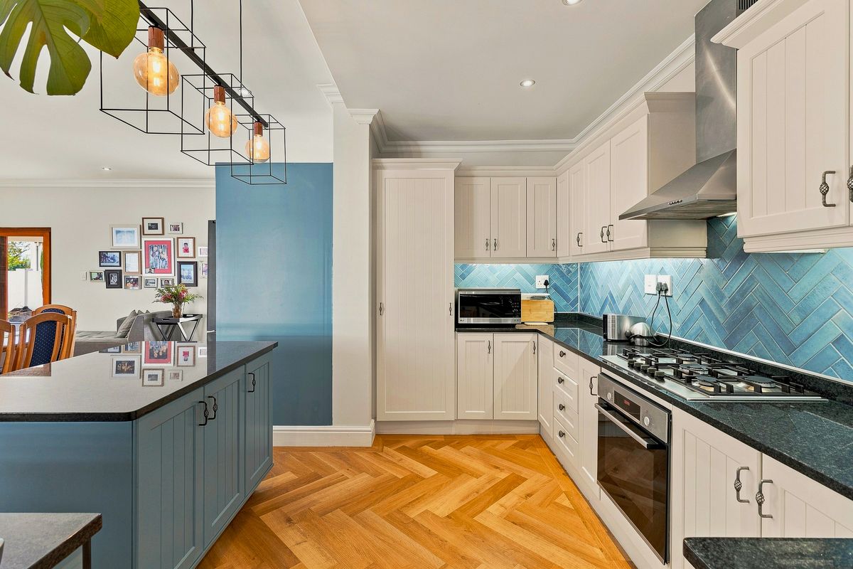 Modern kitchen featuring a central island, herringbone timber flooring, blue herringbone tile backsplash, granite countertops, and high-quality built-in appliances.